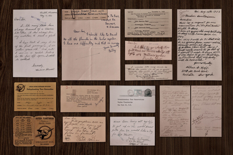 A collection of vintage handwritten letters, notes, and official documents arranged neatly on a wooden surface, including envelopes, postcards, and various types of stationery, showing aged paper and diverse handwriting styles.