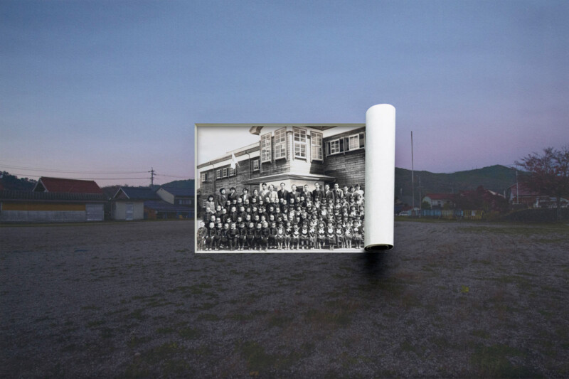 A large black-and-white photo of a group of people in front of a building appears as if unrolled in the middle of an empty outdoor field at dusk, blending past and present scenes.