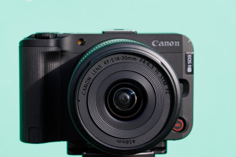 Front view of a Canon EOS R8 camera with a Canon RF 5.1-30mm lens on a turquoise background.