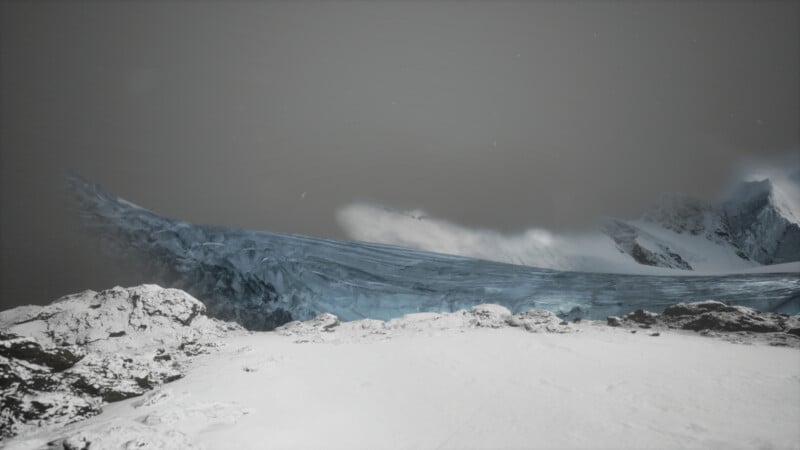 A dramatic, icy landscape featuring a rugged, snow-covered terrain in the foreground. A jagged, blue-gray glacier curves in the distance under a cloudy sky, with towering snow-capped peaks partially visible.