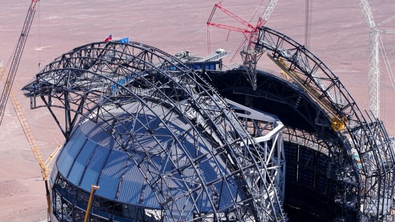 A large, partially constructed steel dome structure with multiple cranes surrounding it at a construction site in a desert landscape.