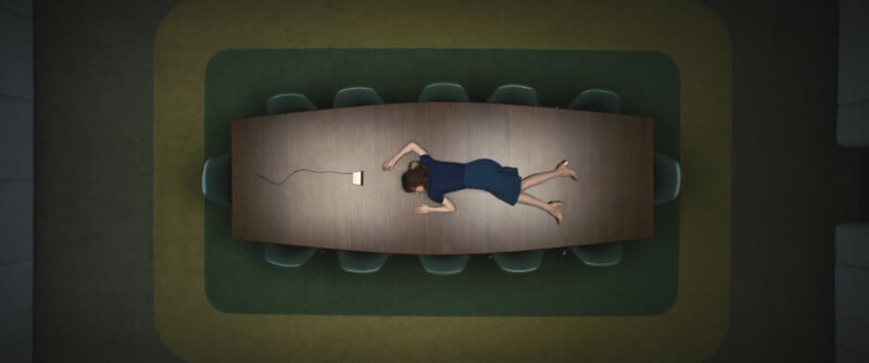A woman in a blue dress lies face down on a long conference table in a boardroom, with a phone and cord nearby; green carpet surrounds the table, seen from an overhead view.