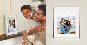 A man smiles while holding a laughing child next to a framed photo of a family. Beside them, a framed photo shows two people hugging and smiling in front of the Golden Gate Bridge.
