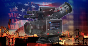 A professional video camera is superimposed over a background of a U.S. flag, financial stock market numbers, and a shipping port with cranes, symbolizing media coverage of economic and trade issues.