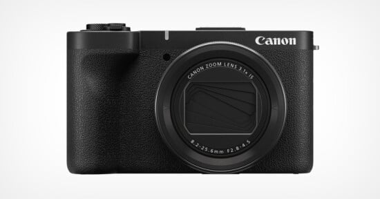 A Canon compact digital camera with a retractable zoom lens and a textured black body. The lens shows specifications, and the brand logo is visible on the top right. The background is plain white.