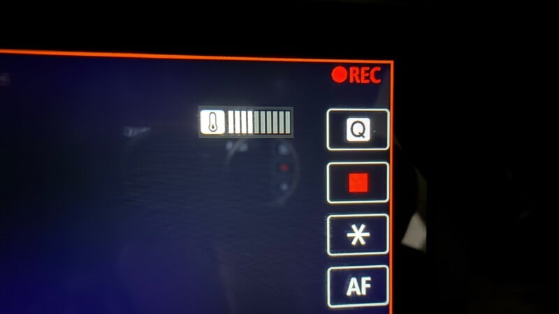 Close-up of a camera screen showing a red "REC" indicator, a temperature icon with a full bar, and buttons labeled Q, a red square, asterisk, and AF, all outlined in white.