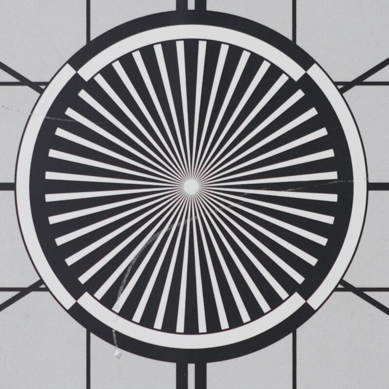 Black and white geometric pattern with a central circle radiating black and white stripes, creating a hypnotic, starburst effect, surrounded by a grid and concentric rings.