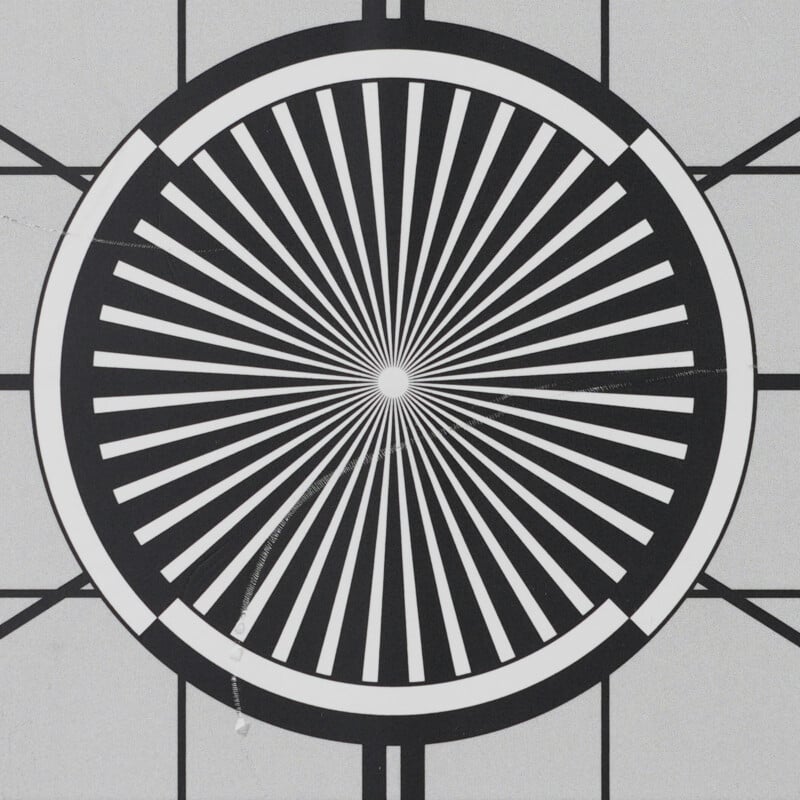 A black and white circular test pattern with radiating spokes, resembling a sunburst, centered within a square background marked by straight lines intersecting at the edges.