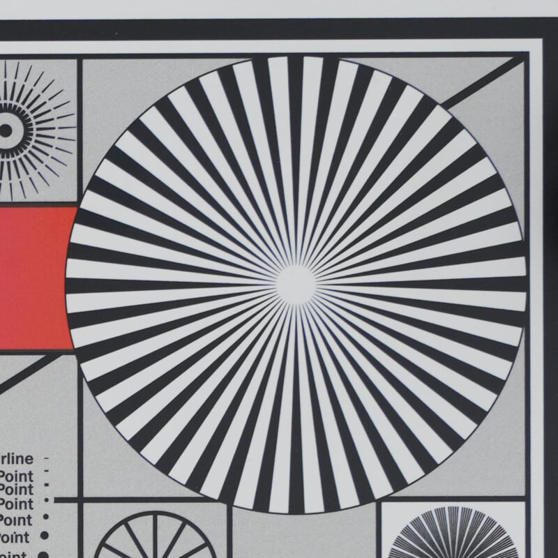A test chart featuring a large black-and-white radial starburst pattern in the center, bordered by geometric shapes and lines, including a red rectangle on the left and smaller patterns around the edges.