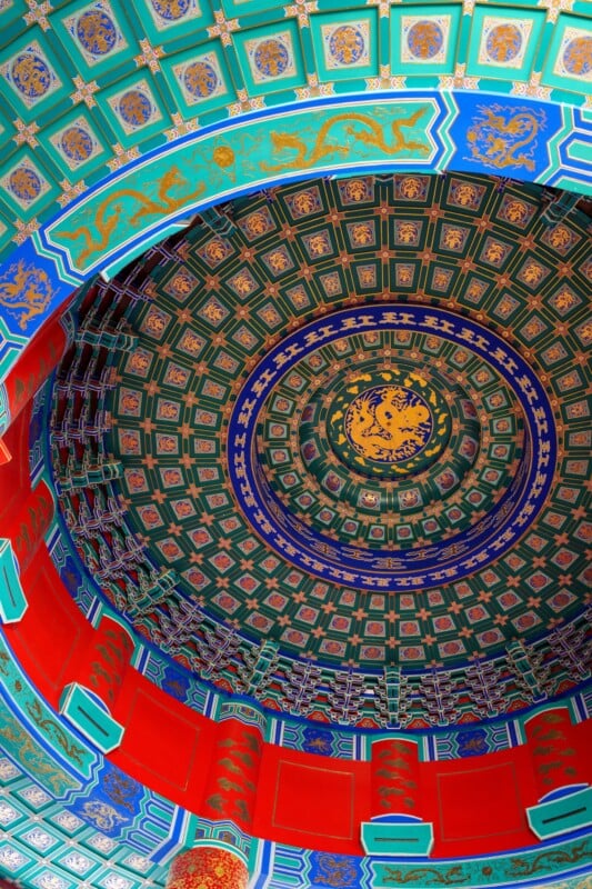 Ornate, colorful ceiling with intricate geometric and floral patterns in green, blue, red, and gold hues. The ceiling has circular layers decorated with traditional Asian motifs, creating a dome-like appearance.