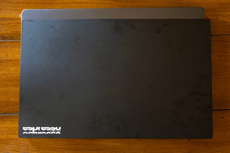 A black laptop partially closed on a wooden table. The corner of the laptop is open, revealing the edge of the screen. The word "espresso" is visible in white on the lower left corner of the laptop's surface.