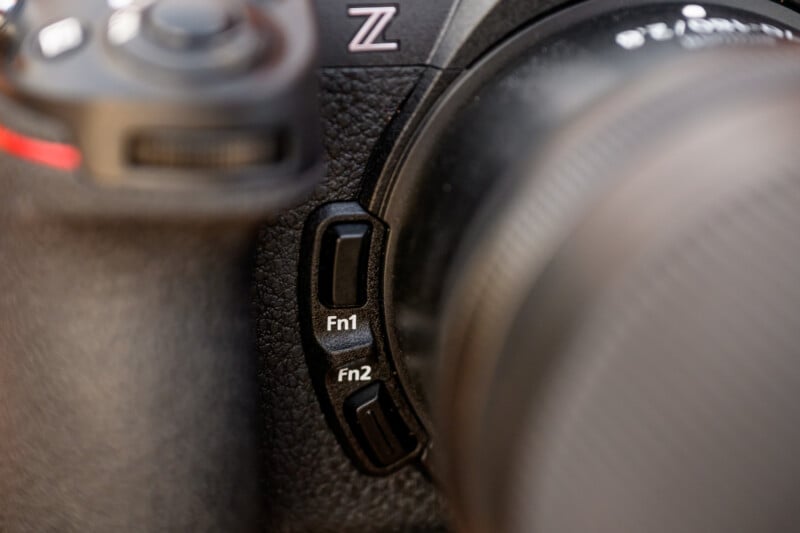 Close-up of a camera showing two customizable buttons labeled "Fn1" and "Fn2" on the left side. The surface has a textured grip, and part of the lens and body are visible.