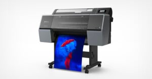A large Epson printer prints a vibrant, high-resolution image of a person in red holding a red umbrella, surrounded by blue smoke against a blue background.