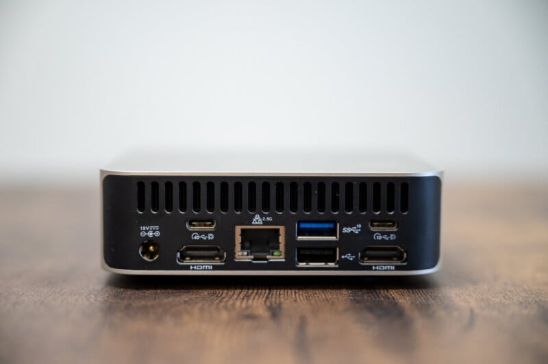 A compact black computer unit with various ports on its back: two USB-C, an Ethernet, two USB-A, and two HDMI ports, against a blurred background.