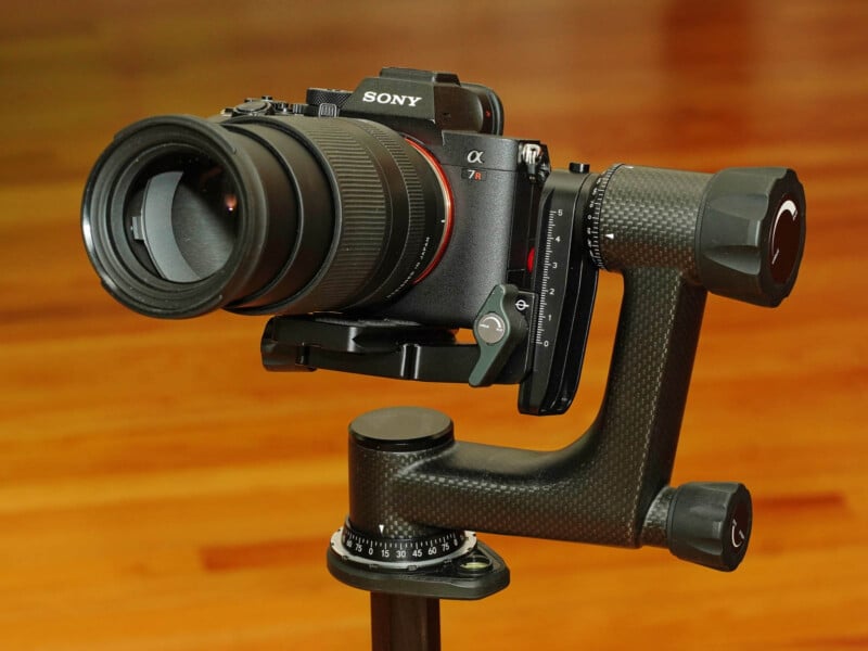 A Sony camera with a large lens is mounted on a gimbal tripod head. The background is a wooden surface.