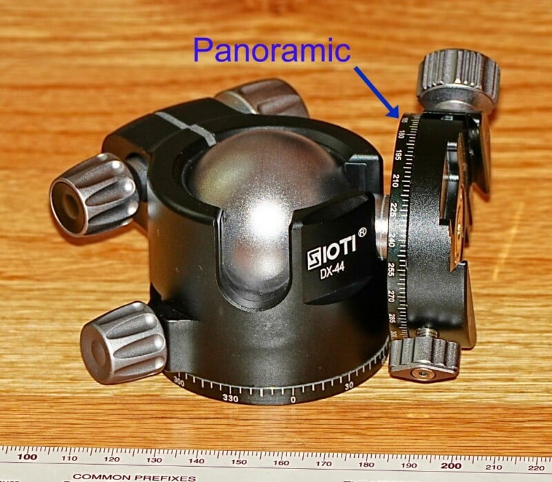 A black Sioti DX-44 panoramic camera tripod head with adjustable knobs and a labeled section marked "Panoramic." A ruler is placed at the bottom of the image for scale.