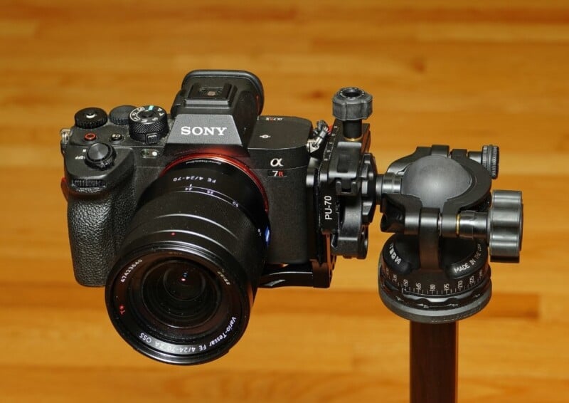 A Sony camera mounted on a PU-70 tripod head, positioned for photography. The camera has a lens attached and is set against a wooden floor background.