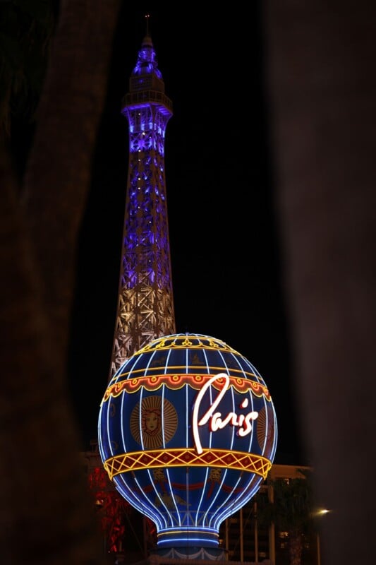 Night view of the illuminated Paris Las Vegas sign, featuring a neon globe with "Paris" written on it, and a replica of the Eiffel Tower glowing with purple and blue lights in the background.