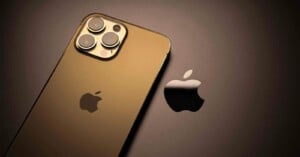 A gold iPhone with triple camera lenses is placed on a surface next to a shiny black Apple logo, both reflecting light and creating a sleek, modern appearance.