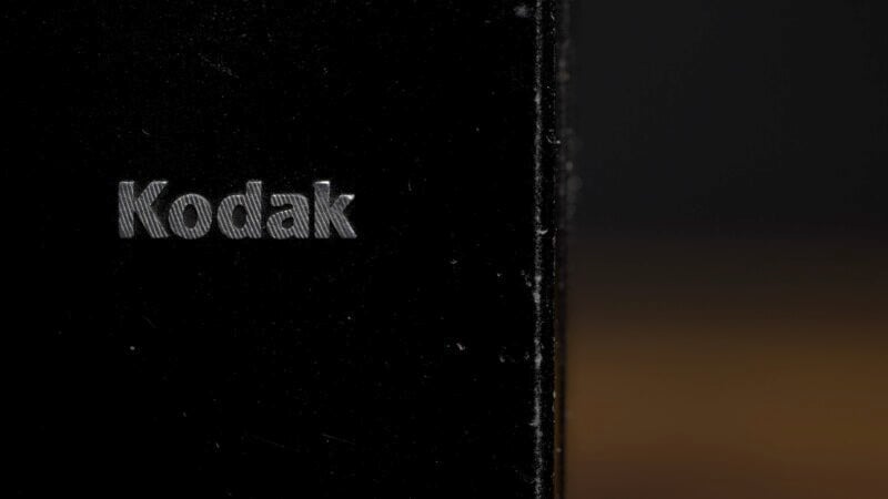 Close-up of the word "Kodak" in metallic letters on a black surface. The background fades into darkness.