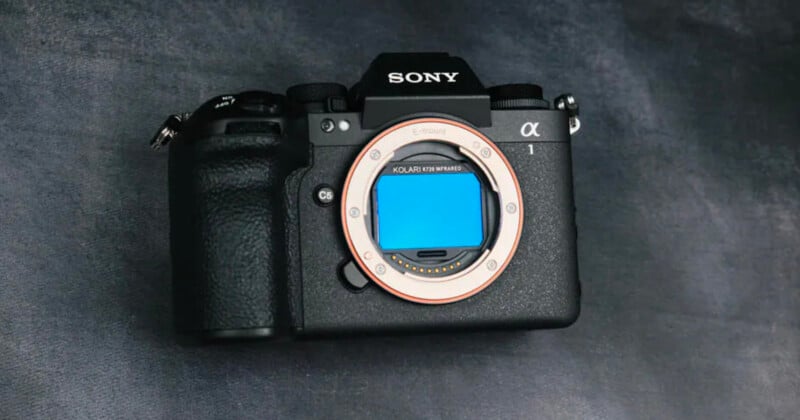 A black Sony Alpha camera body without a lens is placed on a dark textured surface, showing the exposed sensor.