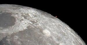 Close-up of the moon's surface showing detailed craters and textures. In the background, a small reddish celestial object, likely a planet or a star, appears on the horizon against a black sky.
