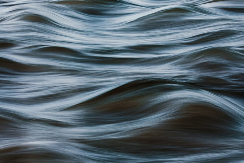 Abstract close-up of moving water with soft, blurred waves and ripples in shades of blue and gray, creating a sense of fluid motion and calmness.