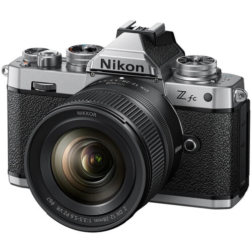 A Nikon Z fc mirrorless camera with a silver and black retro design is shown. It has a textured grip, a prominent lens, and various control dials on top.
