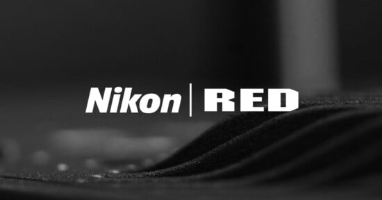 Black and white image showing the words "Nikon" and "RED" in bold white font, separated by a vertical line. The background appears to be a close-up of a textured fabric surface.