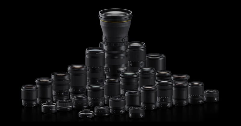 A group of various camera lenses arranged in a semi-pyramid shape on a black background, with one tall lens prominently positioned at the center back.