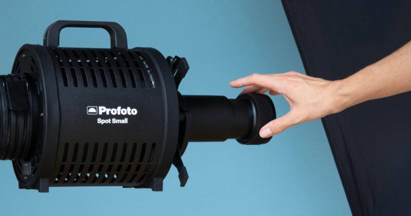 A hand adjusts the front dial of a black Profoto Spot Small studio light against a blue and black background.