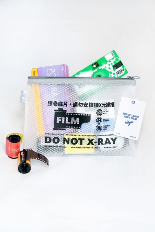 A mesh zipper pouch labeled "FILM DO NOT X-RAY" contains film rolls and boxes, including Kodak and Fujifilm, with a "Travel Safe With Film" card next to it. Two film canisters are placed in front of the pouch.