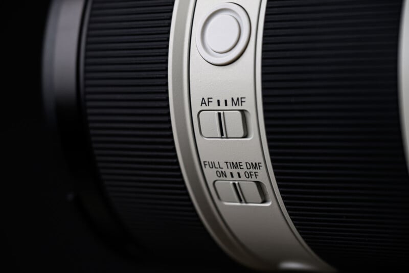 Close-up of a camera lens showing switches for autofocus/manual focus (AF/MF) and full-time direct manual focus (DMF) with ON and OFF positions, set against a black background.