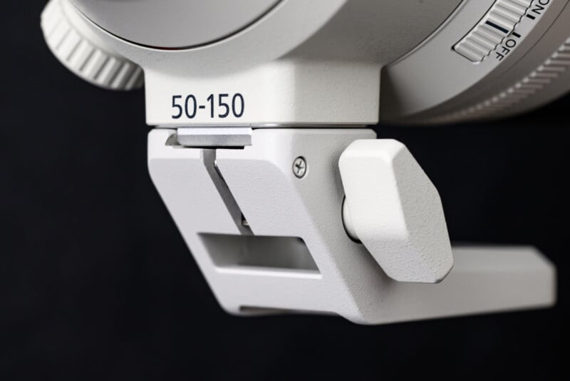 Close-up of a white camera lens mount with a bracket labeled "50-150" against a black background. The image shows detailed texture and mechanical parts of the mounting mechanism.