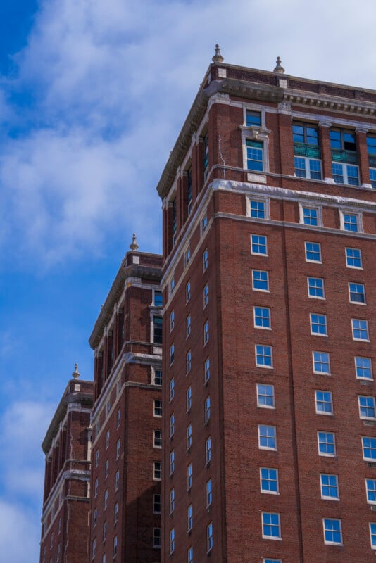 A tall, red-brick building with many windows reaches toward a partly cloudy blue sky. The architecture features decorative stone trim near the rooftop.