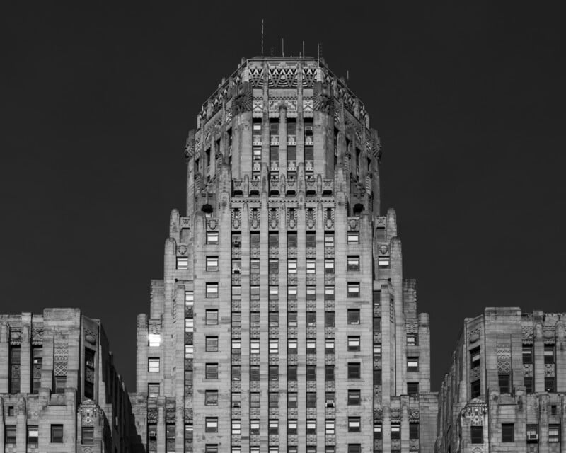Black and white photo of an Art Deco skyscraper with ornate stonework, symmetrical windows, and stepped design rising above lower wings, set against a dark sky.