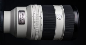 Close-up of a Sony FE 2.8/70-200 GM interchangeable camera lens with a white barrel, black focus and zoom rings, and a metal nameplate, set against a black background.