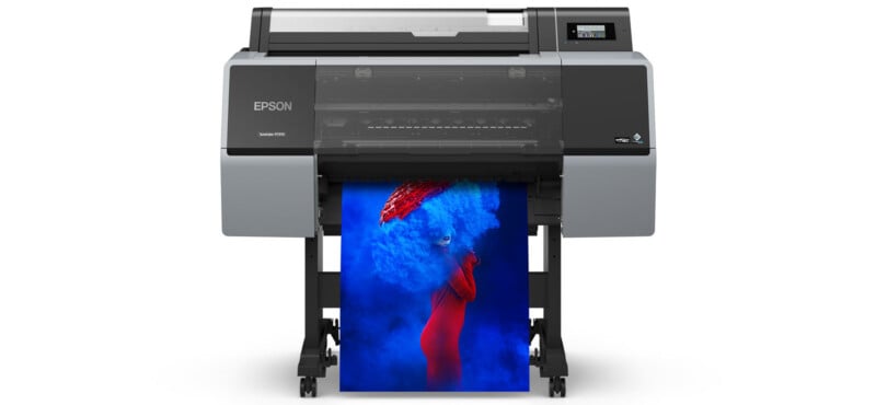 A large Epson printer is printing a vibrant photo of a person in a red outfit surrounded by bright blue smoke, with the image emerging from the printer’s tray.