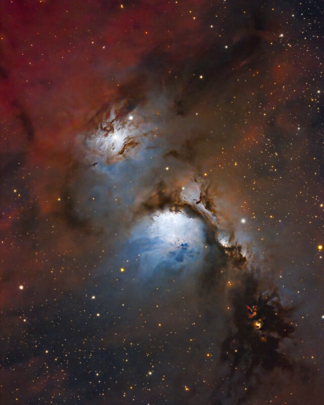A vivid image of deep space shows a colorful nebula with bright blue and white glowing clouds, surrounded by dark dust lanes and scattered stars against a reddish-brown background.