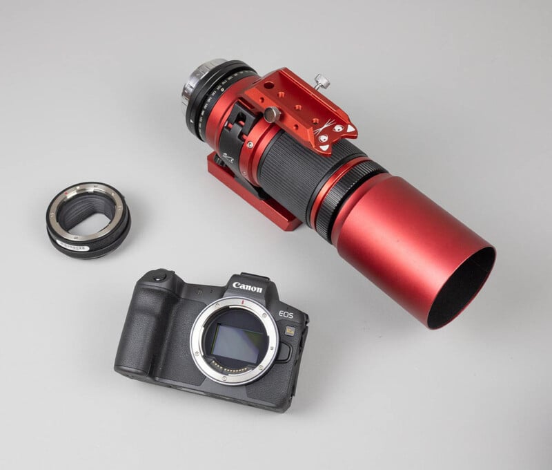 A Canon EOS camera body, a red telephoto lens with a mounting bracket, and a lens adapter are arranged on a light gray surface.