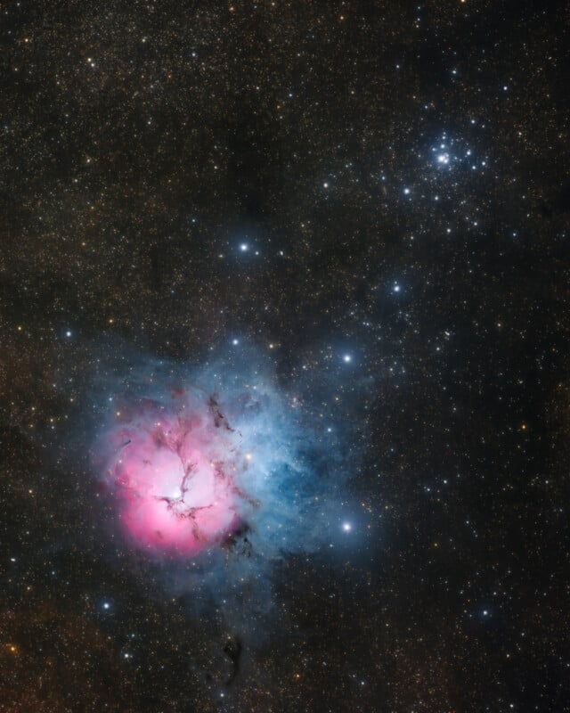 A colorful nebula glows in space with a bright pink and blue core surrounded by dark clouds and countless stars scattered across the background.