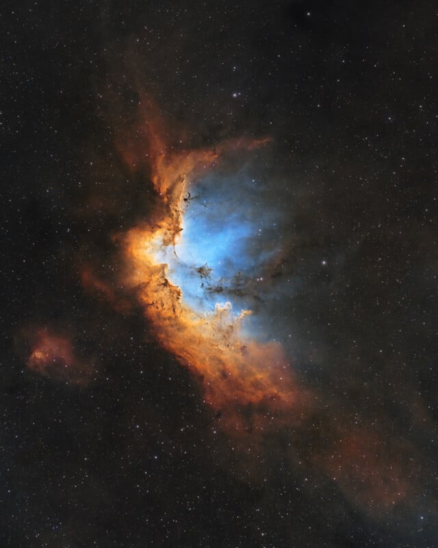Colorful nebula in deep space, featuring bright blue and orange clouds of gas and dust illuminated against a dark, star-filled background.