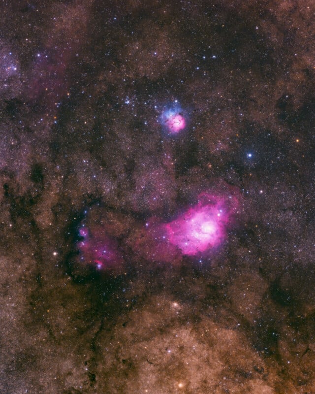 A vibrant image of outer space showing star fields and glowing nebulae, with bright pink and blue clouds of gas against a dark, speckled background filled with countless stars.