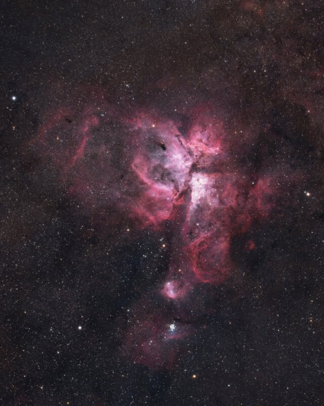 A vivid image of the Carina Nebula shows swirling pink, red, and white clouds of gas and dust illuminated by stars, set against a backdrop of countless stars in deep space.
