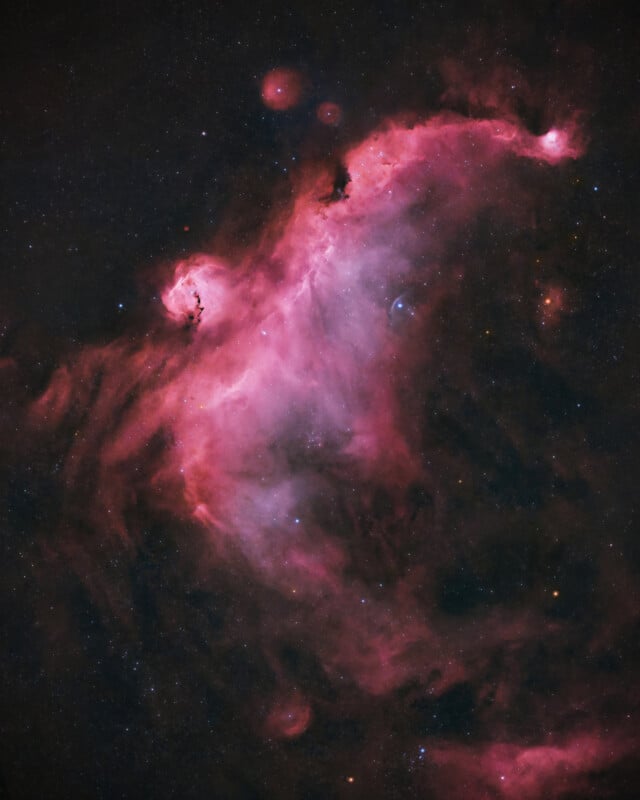 A vibrant space nebula with glowing pink and red clouds of gas and dust, scattered with bright stars against a dark, starry background.