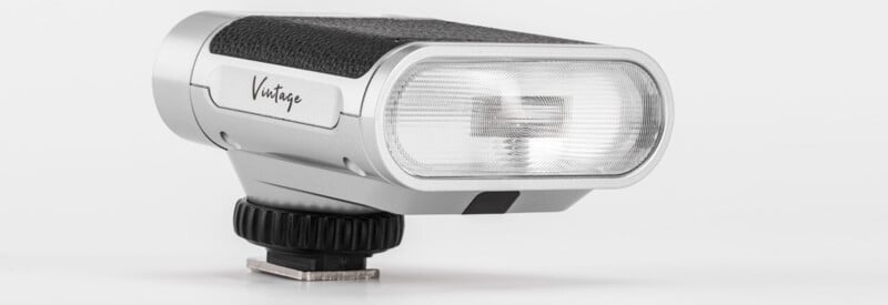 A compact, silver camera flash labeled "Vintage" with a textured black grip, mounted on a hot shoe base, set against a plain white background.