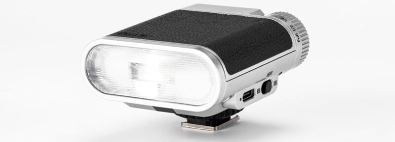 A retro-style camera flash unit with a rectangular front, textured black body, and silver accents, shown against a white background.